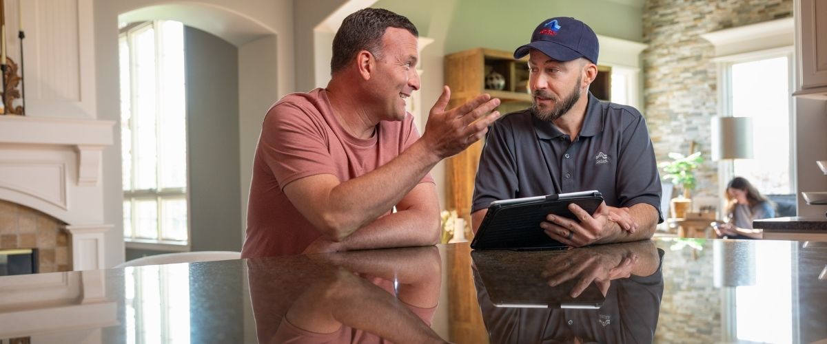 Deux hommes assis à une table de cuisine discutaient en regardant une tablette.