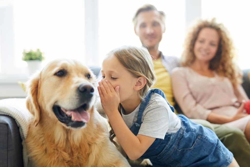 Une fille murmure à l'oreille d'un chien sous le regard de ses parents.