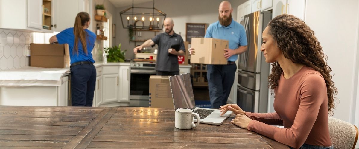 A woman seated at a table, working on a laptop surrounded by several boxes.
