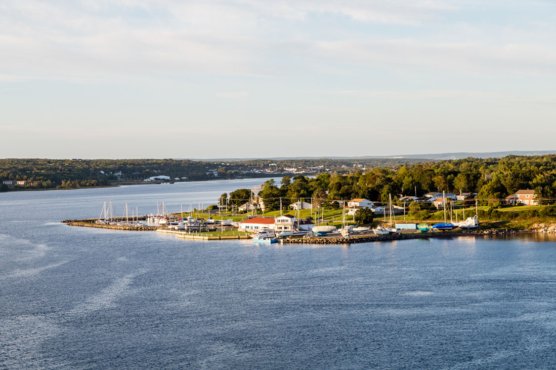Scenic marina in Sydney, Nova Scotia with sailboats and waterfront homes.