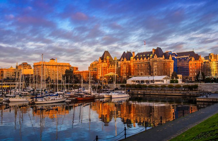 Victoria skyline is mirrored in the calm water, showcasing the city's architecture and natural beauty.