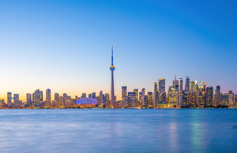 La silhouette de Toronto au coucher du soleil, avec ses bâtiments se détachant sur un ciel aux teintes orange et violettes éclatantes.