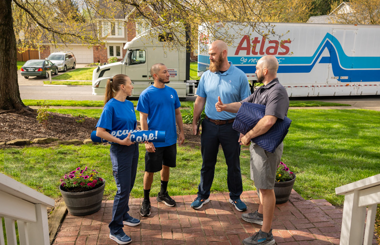 Des agents d'Atlas discutent avec des propriétaires devant leur maison, tenant des fournitures de déménagement près d'un camion Atlas.