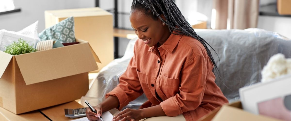 Une femme est assise sur un canapé, utilisant un ordinateur portable tout en tenant un stylo, concentrée sur son travail.