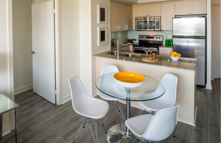 A kitchen featuring a wooden table surrounded by four chairs, with cabinets and appliances in the background.