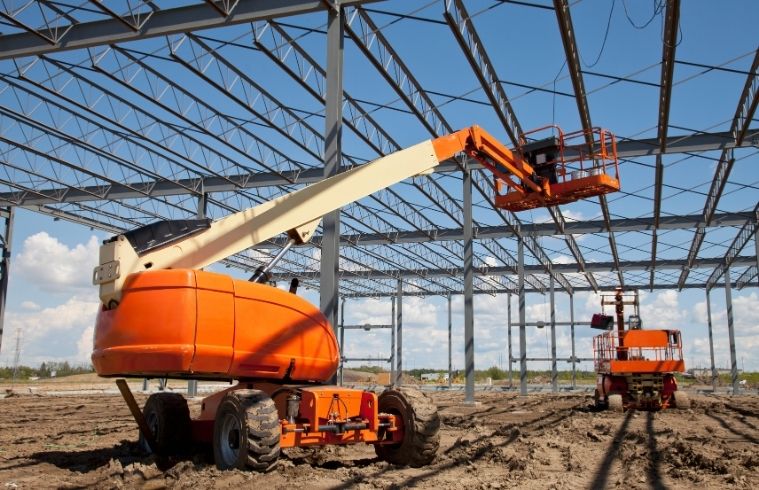 A construction worker in a hard hat is actively working on a building site, surrounded by scaffolding and tools.