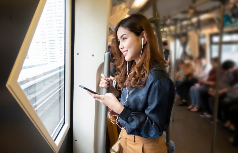 Une femme asiatique assise dans un train, concentrée sur son téléphone portable, avec l'intérieur du train en arrière-plan flou.