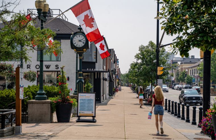 Une femme marche sur un trottoir orné de drapeaux canadiens, créant une ambiance festive.
